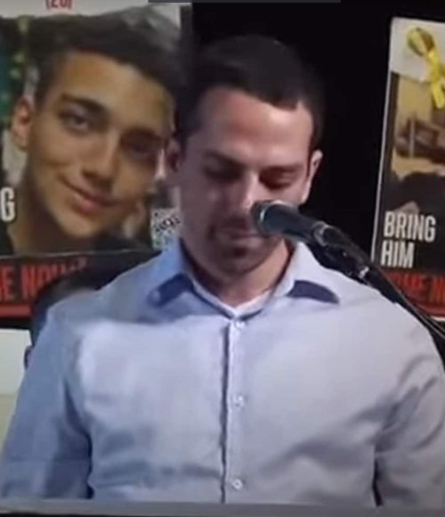 נואם בעצרת שרים יחד לשובם על רקע כרזות החטופים